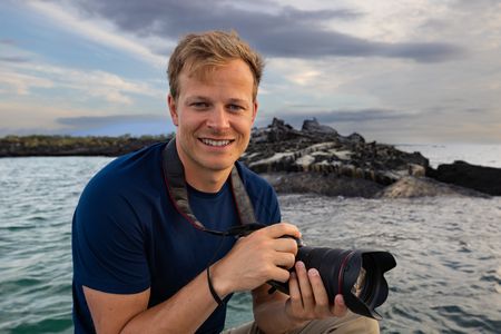 Bertie Gregory photographing Galapagos penguins with marine iguanas.  (credit:  National Geographic/Zubin Sarosh)