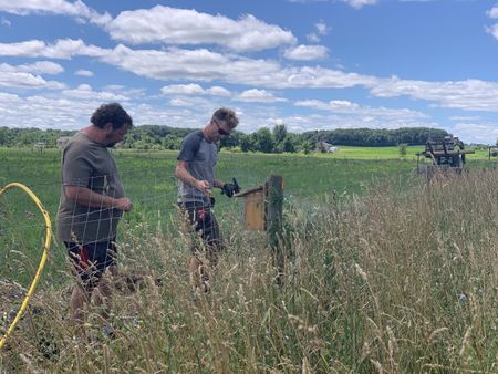 Charles Pol and Scott Brady attach more wire to the Pol family farm's animal pasture fence. (National Geographic)