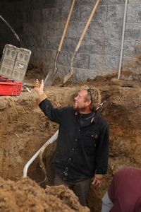 Ben Reinhold smiles at his employee while standing in a hole in the Pol family farm's sheep hut, with Charles Pol, to move the water pipe and provide better drainage of the sheep's excrements. (National Geographic)