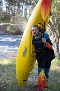 Professional kayaker Ben Stookesberry, wearing kayaking outfit, walks in the woods carrying his kayak and his paddle.  (National Geographic/Harrison Gayton)