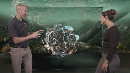 Dr. Mike Heithaus and Dr. Diva Amon speaking in the shark studio lab with the GFX 'Coral' information board centered between them. (National Geographic)