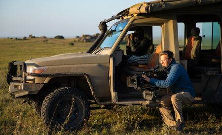 Bertie Gregory sits next to a safari Jeep filming wildlife.  (credit: National Geographic/Jigar Ganatra)