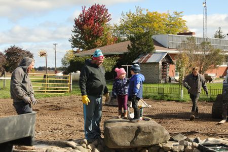 Ben Reinhold smiles at Charles Pol, Abigail Pol, and Levi Reinhold, while Scott Brady walks by, at the Pol family farm's pond in their new garden. (National Geographic)