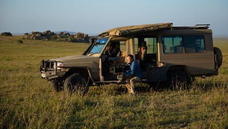Bertie Gregory sits next to a safari Jeep filming wildlife. (credit: National Geographic/Jigar Ganatra)