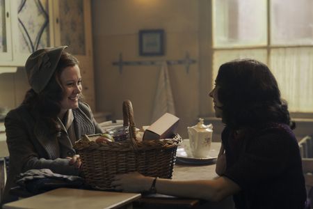 A SMALL LIGHT - Lotte, played by Lisa Karlstrom, gives Miep, played by Bel Powley, a care package for her husband Pfeffer as seen in A SMALL LIGHT. (Credit: National Geographic for Disney/Dusan Martincek)