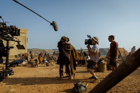 The crew films Frankie Treadaway (Avianius), Theo Ogundipe (Marcus Masurius) and Angelina Chudi (Aurelia Masuri) during a reunion scene at the Pompeii displacement camp, behind-the-scenes of Pompeii: Out of Time with Tom Hiddleston. (National Geographic/Darrin Zammit Lupi)