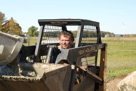 Charles Pol drives the compact track loader the team is using to transport wet concrete for the sheep hut's flooring. (National Geographic)