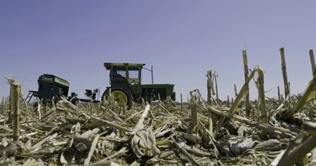 Charles Pol drives a green tractor through the corn field that they trying to convert into a hayfield. He is about to get stuck in the mud. (National Geographic)