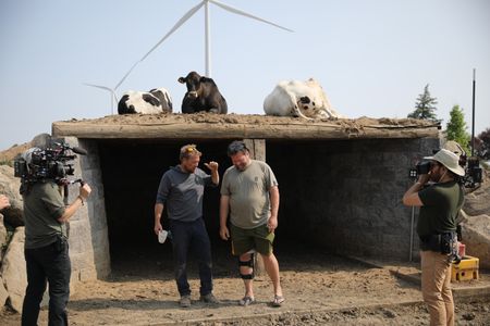 Two crew members film Ben Reinhold and Charles Pol chatting in front of the sheep hut while three cows lay on top of it at the Pol family's farm. (National Geographic)