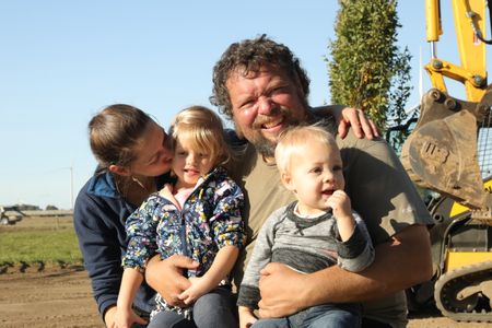 Beth Pol kisses Abigail Pol while sitting on Charles Pol's lap with Silas Pol, at the Pol family farm's new pond. (National Geographic)