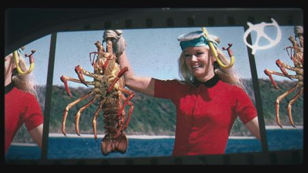 Valerie Taylor in red swimsuit holding up a crayfish, 1968. (photo credit: Ron & Valerie Taylor)