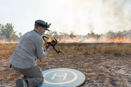 Drone operator Jack Richardson preparing an FPV drone for take off to film a burning savanna. (National Geographic/Sacha Thorpe)