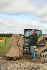 Charles Pol stands by a large rock that was transported from the front yard to the Pol family farm's new pond to be used as a centerpiece. (National Geographic)