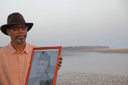 Stephen Woodson holds a picture of his father, Waverly Woodson Jr., while standing on Omaha Beach in France. Waverly Woodson Jr. was a combat medic who served with the 320th Barrage Balloon Battalion on D-Day. (National Geographic/Shianne Brown)