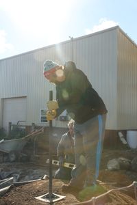 Charles Pol uses a tamper to level out the dirt pile that will become a waterfall for the Pol family farm's pond while Ben Reinhold watches. (National Geographic)