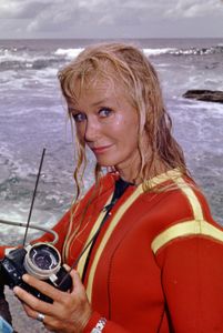 Valerie Taylor in red wetsuit posing with camera equipment. (photo credit: Ron & Valerie Taylor)