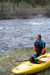 Professional kayaker Ben Stookesberry kneels by the river with his kayak and paddle.  (National Geographic/Harrison Gayton)