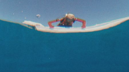 Valerie Taylor leaning over the boat looking into water in 1968. Shot from underwater. (photo credit: Ron & Valerie Taylor)