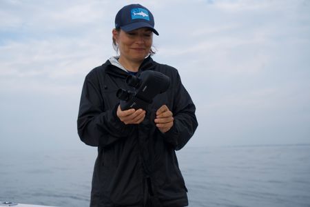 Dr. Alisa “Harley” Newton stands on the front of the teams boat, preparing a pair of binoculars, to start searching for Liberty's tag. (National Geographic/Brandon Sargeant)