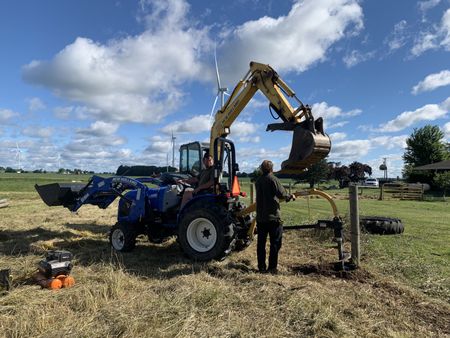 Charles Pol sits in the blue tractor and Andrew Hutton sits in the yellow tractor, while Ben Reinhold holds the auger to create a hole for a post that will hold up the animal pasture's fence. (National Geographic)