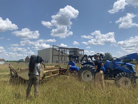 Two crew members film Charles Pol and Dr. Pol attaching a mower conditioner to a tractor at the Pol family's farm. (National Geographic)