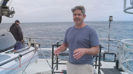 Ryan Johnson, expert, demonstrating how the rig device he has created will be utilized in their upcoming experiment to help measure the size and speed of the particular great white shark in the water. (National Geographic)
