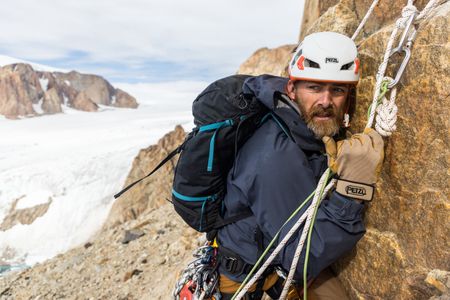 Aldo Kane hugs the rock during an ice fall on the Pool Wall in Eastern Greenland.  (photo credit: National Geographic/Matt Pycroft)
