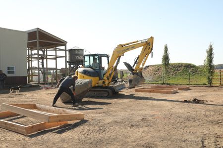 Ben Reinhold and Andrew Hutton move a large centerpiece rock to the Pol family farm's new garden using a mini excavator. (National Geographic)