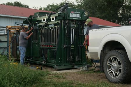 Terry Rohan tries to sooth his bull that is inside the chute as Dr. Ben prepares to treat the bull's foot after he has calmed down. (National Geographic)