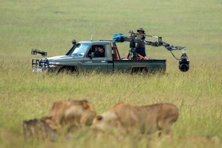 Faith Musembi stands in the back of the film vehicle, swinging the jib of the GSS camera as the crew captures Summer's Pride in action in the foreground. (National Geographic/Abigail Brown)