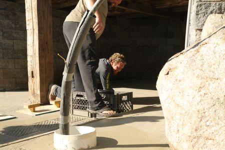 Ben Reinhold smiles as he smooths out the sheep hut floor's wet concrete while Charles Pol uses plastic crates to create grooves that will provide better drainage of the sheep's excrements. (National Geographic)