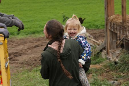 Beth Pol holds Abigail Pol as she smiles out front of the old barn the family is taking down. (National Geographic)