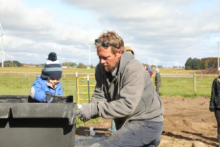 Levi Reinhold assists Ben Reinhold with gluing the water tank for the Pol family farm's pond in their new garden. (National Geographic)