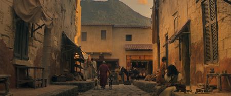 Avianius crosses a street lined with market stalls, passing a man leading two goats, as Vesuvius looms in the background in Pompeii AD 79, prior to the eruption. (National Geographic)