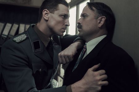 A SMALL LIGHT - Silberbauer, played by Daniel Donskoy, threatens Kugler, played by Nicholas Burns, as seen in A SMALL LIGHT. (Credit: National Geographic for Disney/Dusan Martincek)