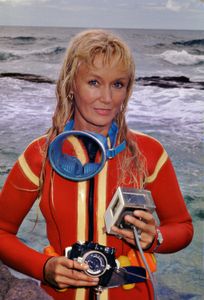Valerie Taylor in red wetsuit posing with camera equipment. (photo credit: Ron & Valerie Taylor)