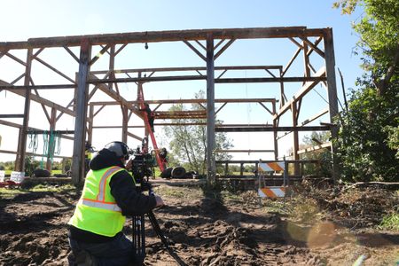 Ben Reinhold climbs a ladder, held by Charles Pol, to take down the remaining beams of the old barn, while a crew member films. (National Geographic)