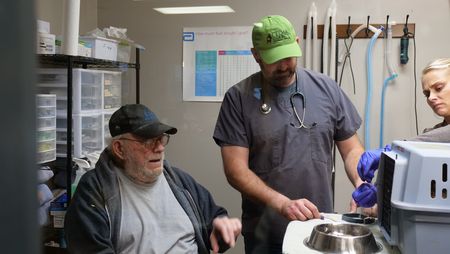 Owner Jesse Robinett waits as Dr. Ben Schroeder and vet tech Val Sovereign gets his cat Tomcat back into a crate to head home. (National Geographic)