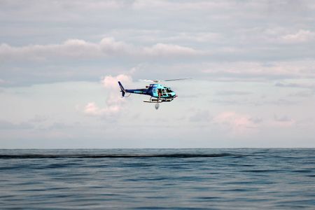The helicopter flies over the water with Aldo Kane holding out a net. (National Geographic/Mario Tadinac)