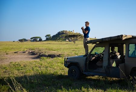 Bertie Gregory stands on the front bonnet of a safari Jeep looking for animals. (credit: National Geographic/Jigar Ganatra)