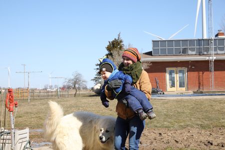 Beth Pol holds her son, Silas Pol, as they make their way to check on the newly born lambs, accompanied by Clovis, the Pol family's dog. (National Geographic)