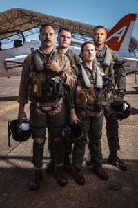 Students LTJG Spenser Neel, LTJG Dylan Horan, Captain Steph Harris, and Captain Micah Nissly pose together in front of a T-45. (Credit: National Geographic/Freddie Claire)