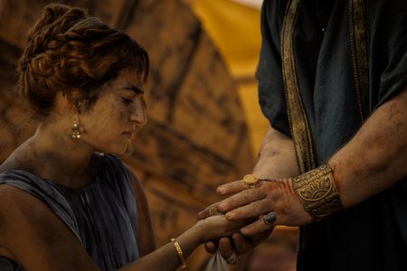 At the Pompeii displacement camp, Cassius, played by Robert Bowman, hands the money he owed to Julia Felix to Amalthea, played by Buket Komur. (National Geographic/Darrin Zammit Lupi)