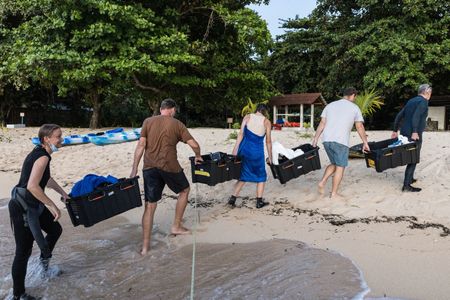 Secrets of the Octopus team members, Yvonne Press, Jaap Barendrecht, Jordan Pert, Woody Spark, and Rory McGuinness, working together to unload equipment from the dive vessel to be cleaned and prepped again for the next day of filming Algae octopus (Abdopus aculeatus).  (photo credit: National Geographic/Harriet Spark)