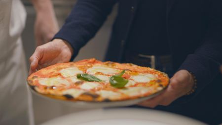 Ramadan El Sabawy hands Stanley Tucci a plate with his son's crispy, mouthwatering Margherita Pizza.(credit: National Geographic)
