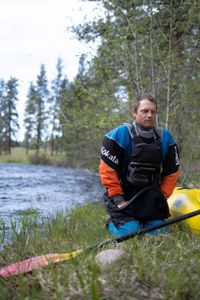Professional kayaker Ben Stookesberry kneels by the river with his kayak and paddle.  (National Geographic/Harrison Gayton)