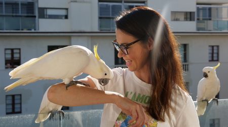 Suzy Roessel standing on her balcony with a cockatoo on her arms. (Big Wave Productions)