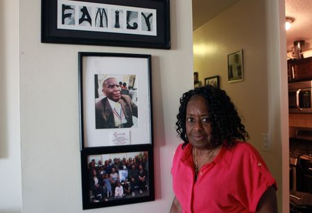 Claudette Simmons poses for a photo next to a portrait of her father, Clark Simmons, in her home in New York. "Erased: WW2's Heroes of Color" tells the stories of three Black heroes who miraculously survived the attack on Pearl Harbor. One of these men was Clark Simmons, who served as mess attendant on the USS Utah. (National Geographic/Nelson Adeosun)