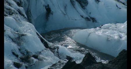 Stream runs down glacial ice covered in volcanic ash.  (credit: National Geographic)