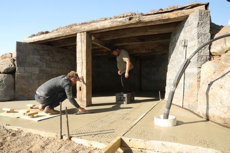 Ben Reinhold smooths out the sheep hut floor's wet concrete as Charles Pol uses plastic crates to create grooves that will provide better drainage of the sheep's excrements. (National Geographic)